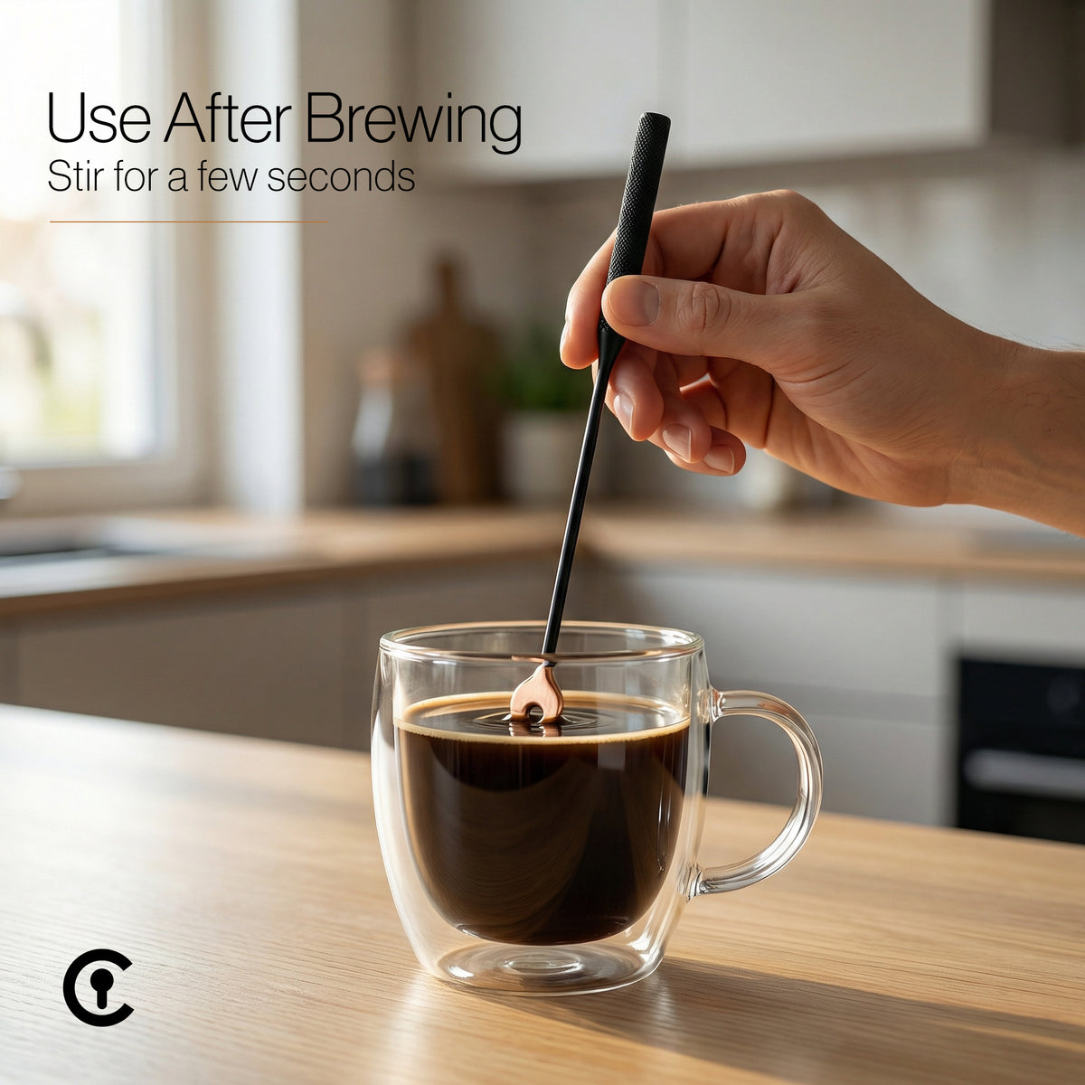 Person stirring coffee with the Coffee Key in a clear mug with a kitchen background