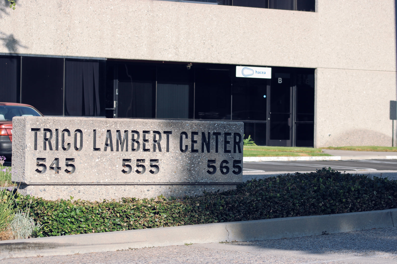 Concrete monument sign showing "Trico Lambert Center" with Hacea Coffee Source sign in the background.