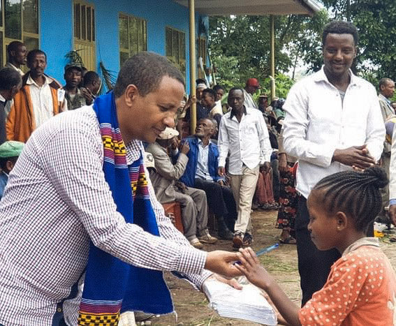 Faysel Yonis shaking hands with a young girl in an outdoor setting with other people in the background.